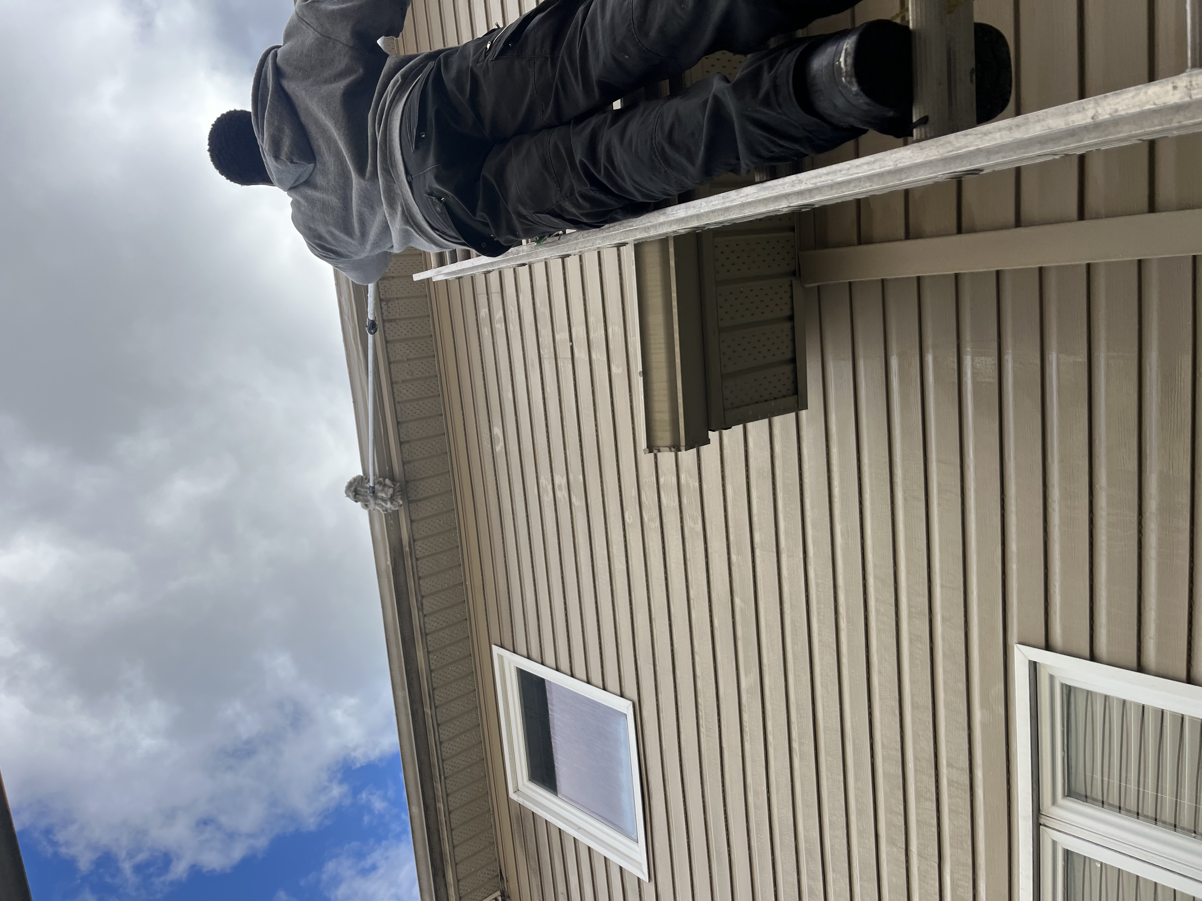 HomeShowers team member cleaning eavestroughs on a ladder in Ottawa